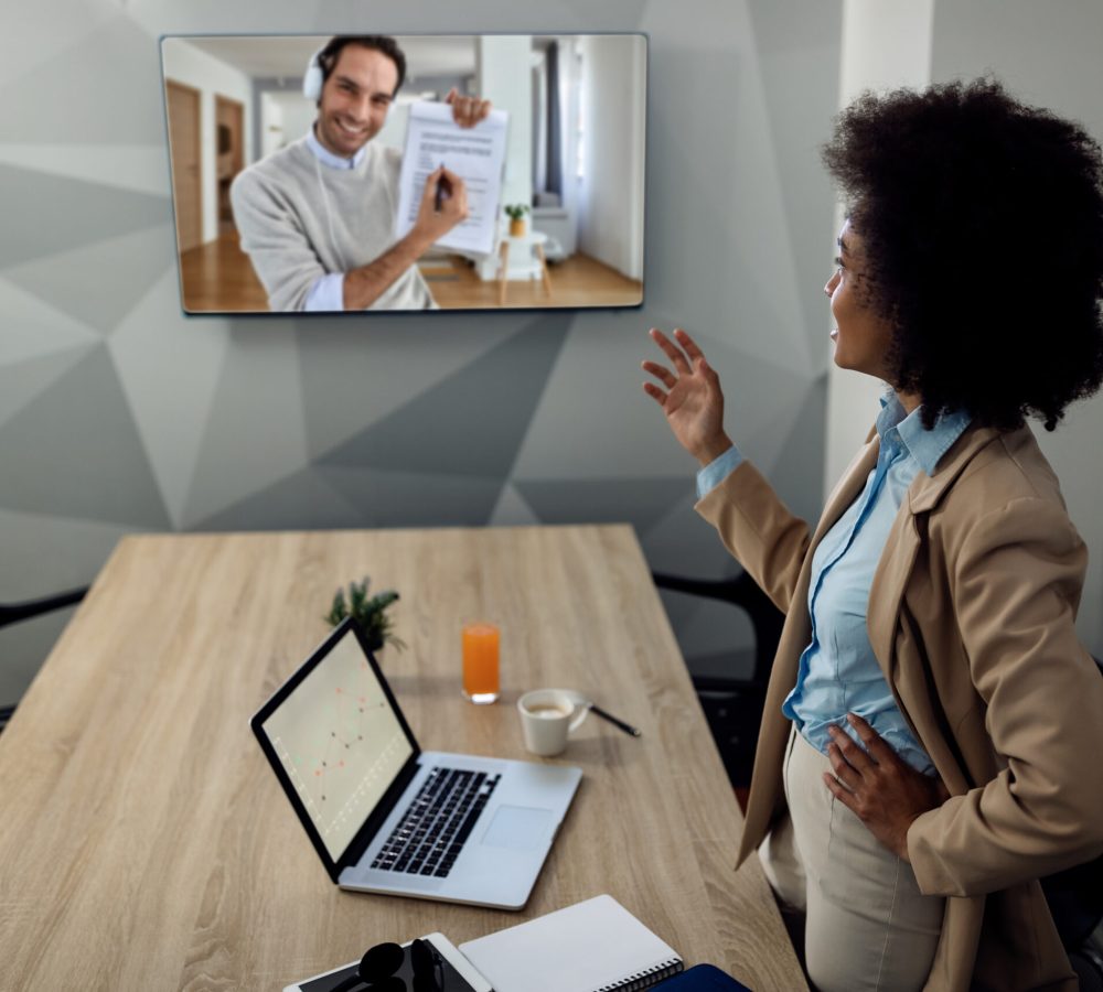 Black businesswoman talking with male coworker through video call while working in the office.